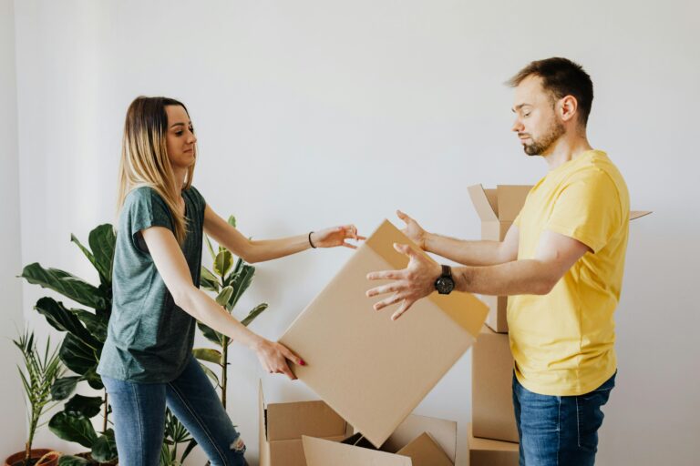 Side view serious couple wearing jeans and shirts carrying cardboard boxes with belongings while moving into new apartment together